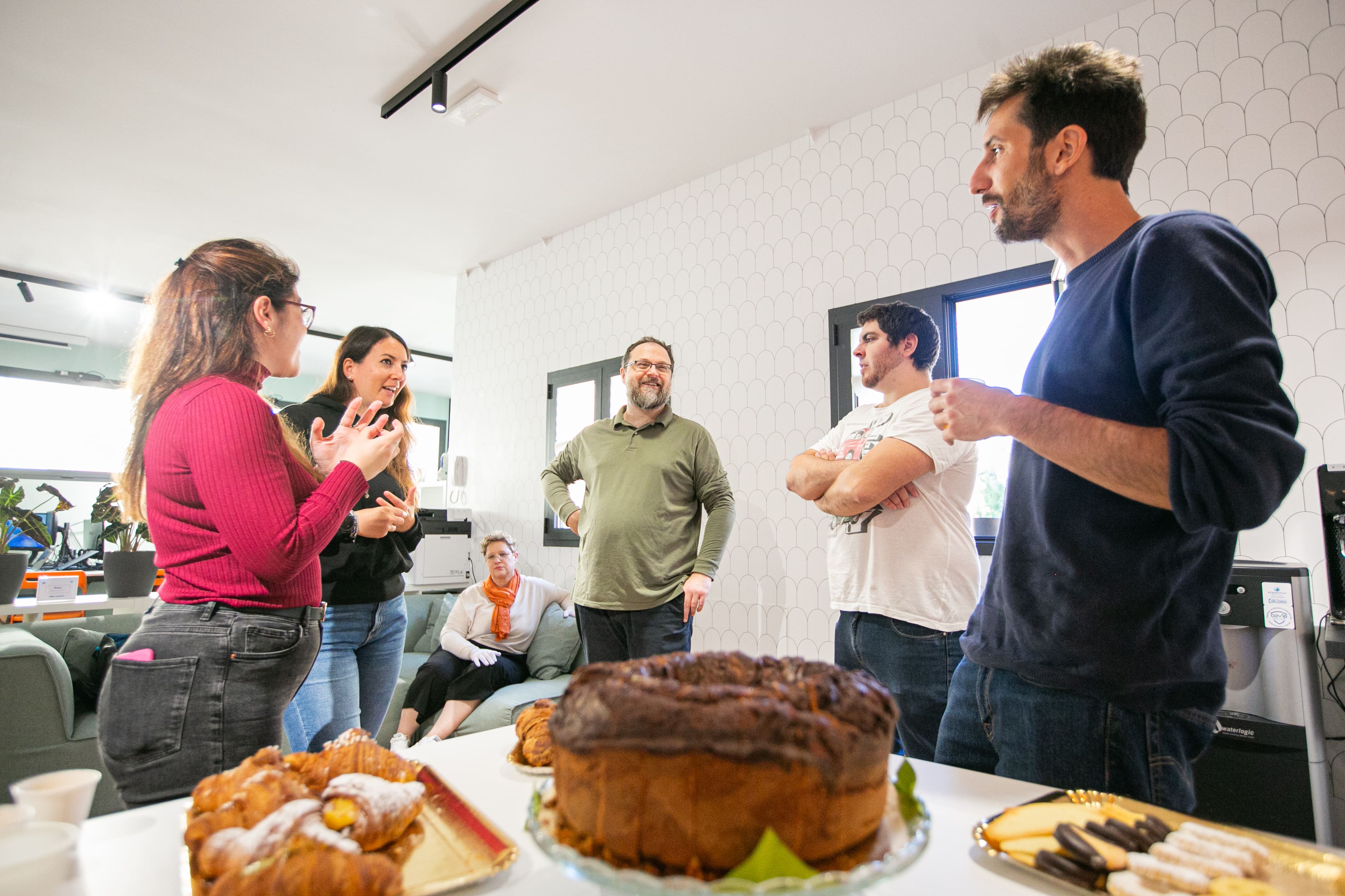 Alcuni membri del team Nephila, sereni e sorridenti, riuniti attorno a un tavolo imbandito di bevande e prelibatezze scambiano due chiacchiere prima di passare alle attività in programma per il retreat.