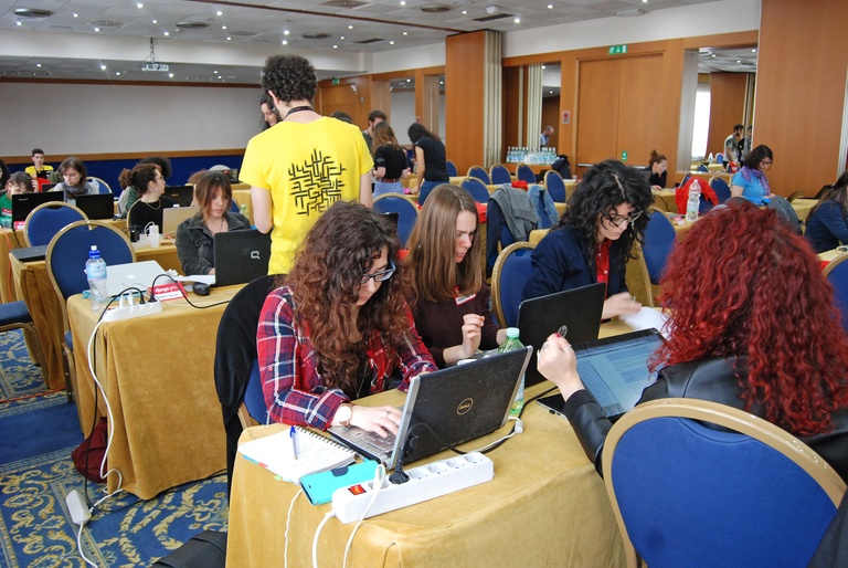 A group of people working on laptops at tables in a conference room.
