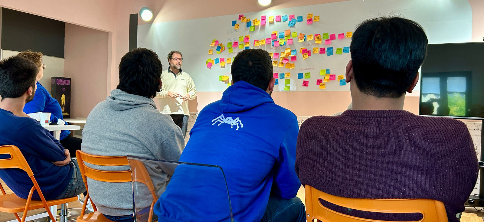 Durante un workshop, cinque persone del team Nephila sono sedute su sedie arancioni di fronte a una lavagna con attaccati tanti post-it.