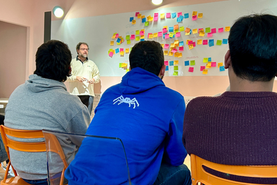 Durante un workshop, cinque persone del team Nephila sono sedute su sedie arancioni di fronte a una lavagna con attaccati tanti post-it.